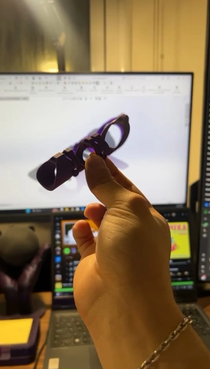 Mano sosteniendo una pieza impresa en 3D de una férula de dedo, delante del modelo en pantalla